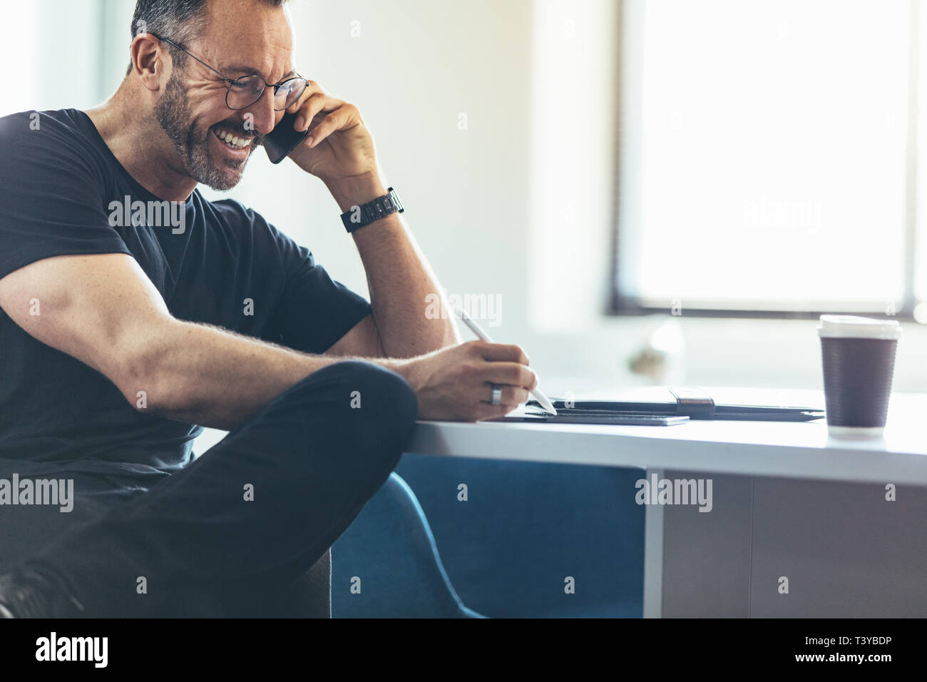 Unternehmer im Gespräch über Handy und der Arbeit an seinem digitalen tablet, während an seinem Schreibtisch sitzen. Geschäftsmann mit Mobiltelefon und lächelnd im Büro Stockfoto