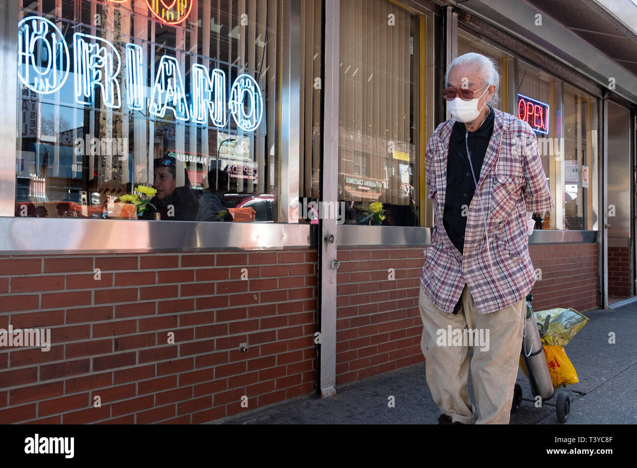 Eine ältere asiatischer Mann zu Fuß auf Roosevelt Ave in Jackson Heights, während das Tragen einer Maske und zu einer Sauerstoff Tank angebracht. In Queens, New York. Stockfoto