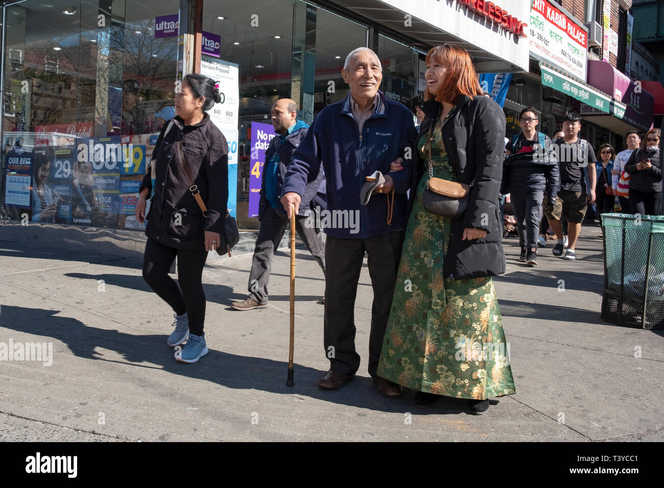 Eine junge asiatische Frau geht Arm in Arm mit einem älteren Mann, vermutlich ihr Großvater. Auf 74th St. in Jackson Heights, Queens, New York City. Stockfoto
