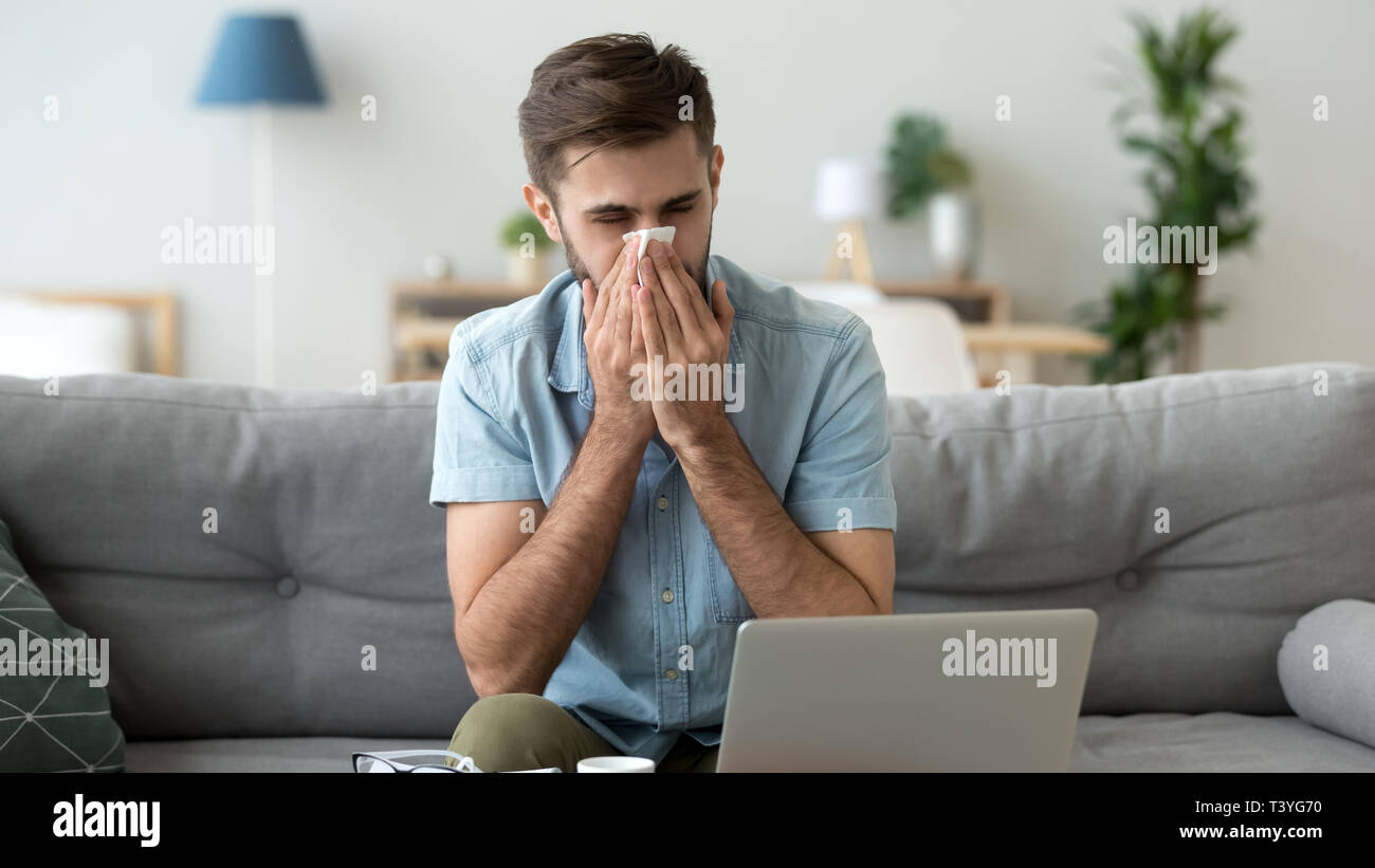 Kranken Mann blasen Nase, Taschentuch, mit Laptop zu Hause Stockfoto