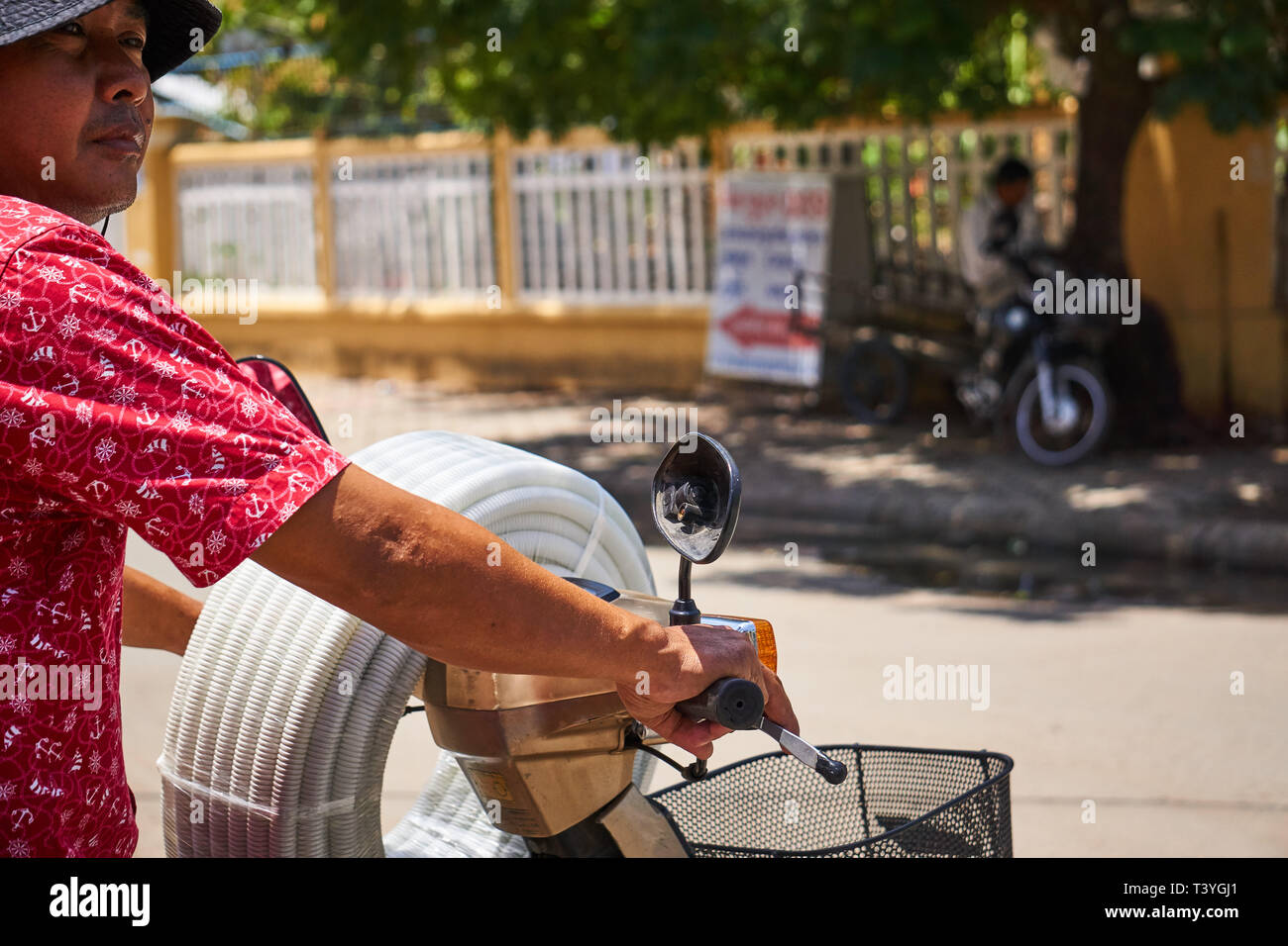 Ein kambodschanisches Mann reitet ein Moped (Motorrad, Motorroller) auf den Straßen von Phnom Penh, Kambodscha, mit Rohren um den Lenker gewickelt. Stockfoto