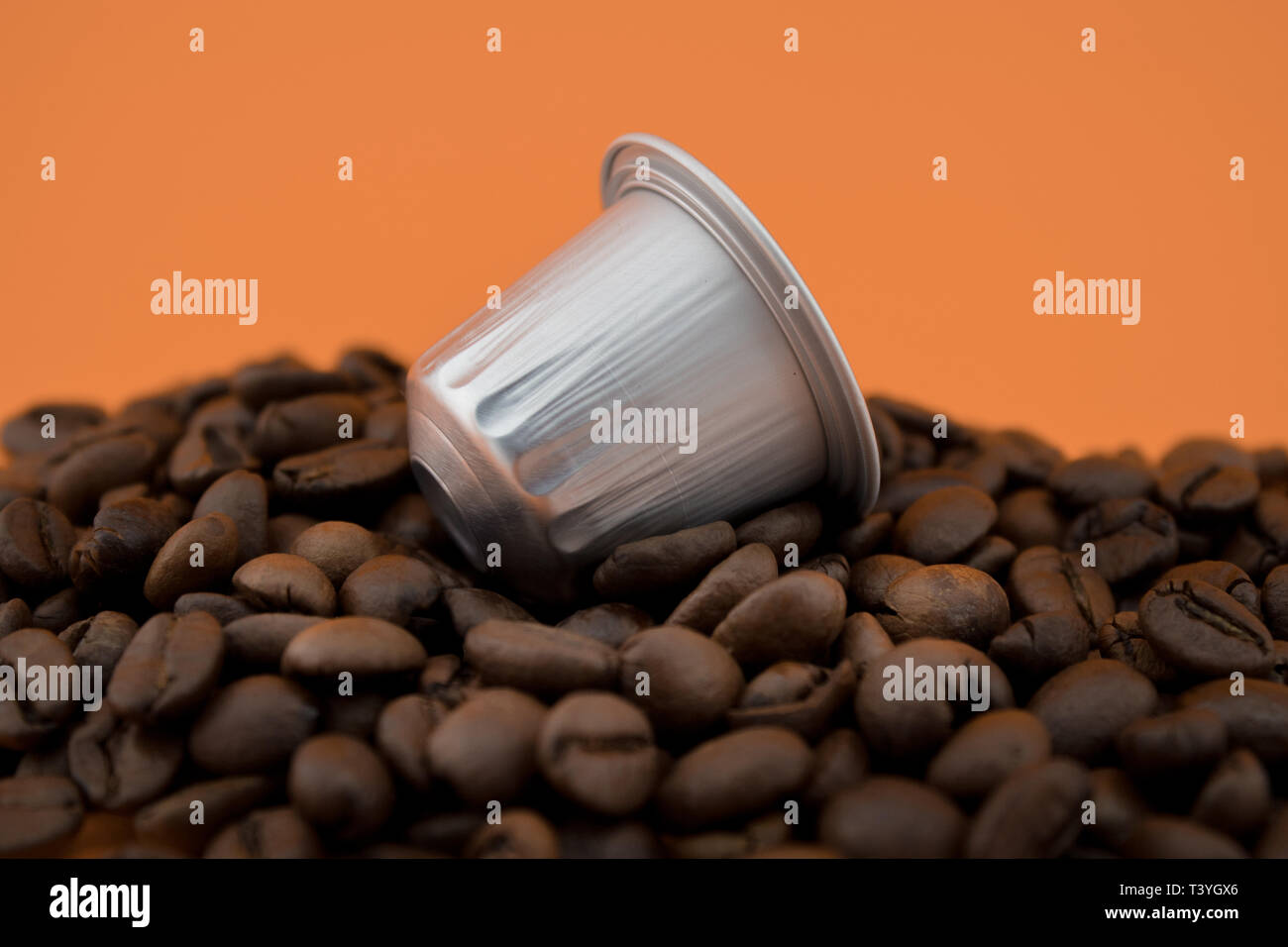 Espresso Kapsel oder kaffeepad auf Kaffeebohnen, orange hinterlegt. Kapseln für die Kaffeemaschine. Stockfoto