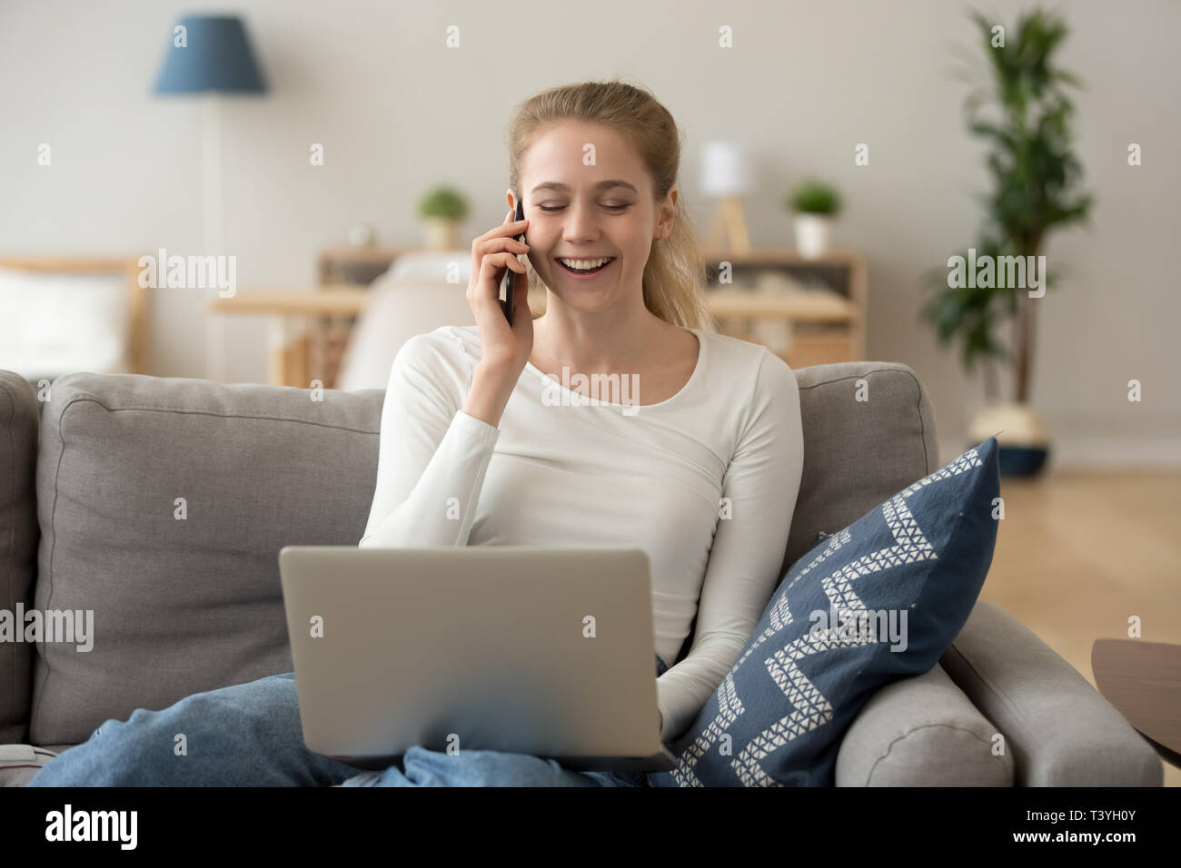 Lachende Frau am Telefon sprechen, sitzen auf der Couch, mit Laptop Stockfoto