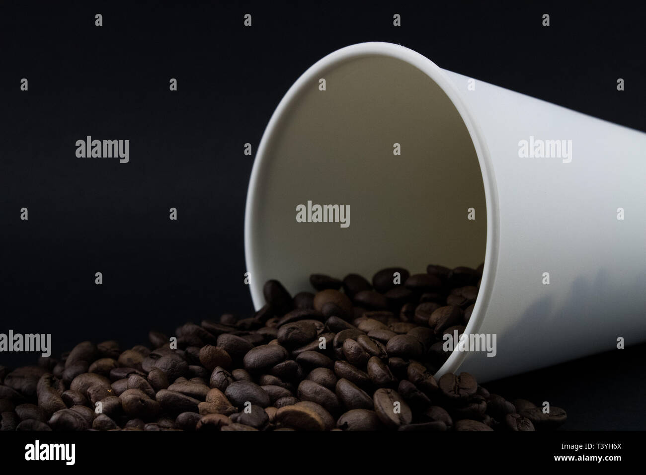 Take-out Kaffeetasse mit dem verschütteten Kaffee Bohnen, schwarzen Hintergrund. Geröstete Kaffeebohnen. Stockfoto
