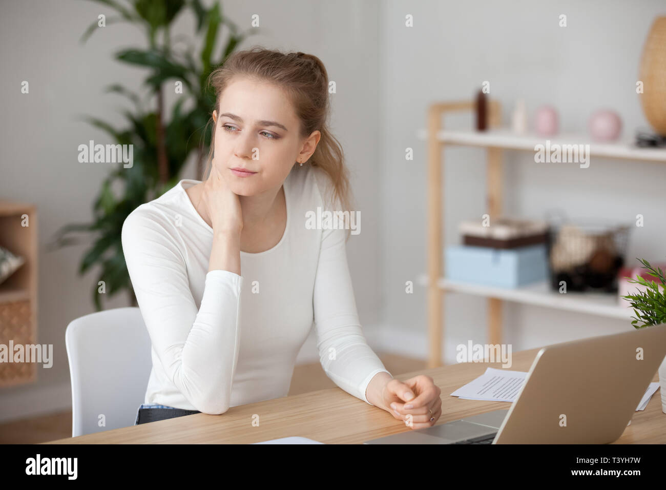 Nachdenkliche Frau vor dem Laptop sitzend, in Gedanken verloren Stockfoto