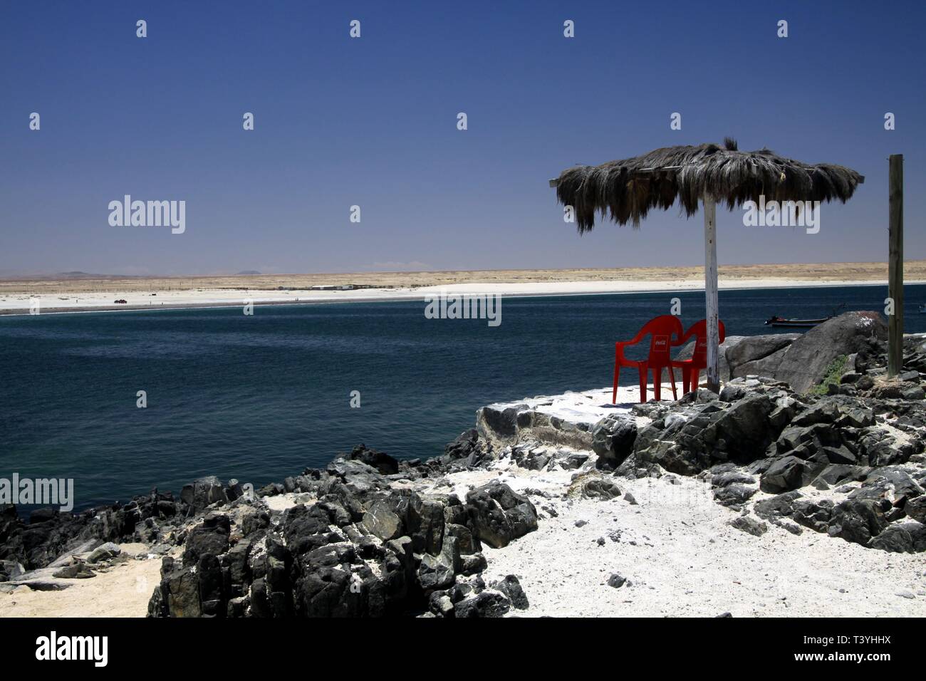 White Sand Beach (Playa Blanca) an der pazifischen Küste von Atacama Wüste mit isolierten roten Plastikstühlen unter Reet reed Regenschirm Stockfoto