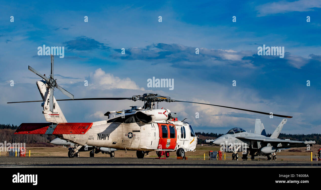 190329-N-KL 795-1003 Whidbey Island, WA (29. März 2019) einen NAS Whidbey Island MH-60S Suche und Rettung Hubschrauber sitzt in der Nähe von EA-18G Growler von VAQ-130 an Ault Feld. (U.S. Marine Foto von Chief Mass Communication Specialist Paul Seeber/Freigegeben) Stockfoto