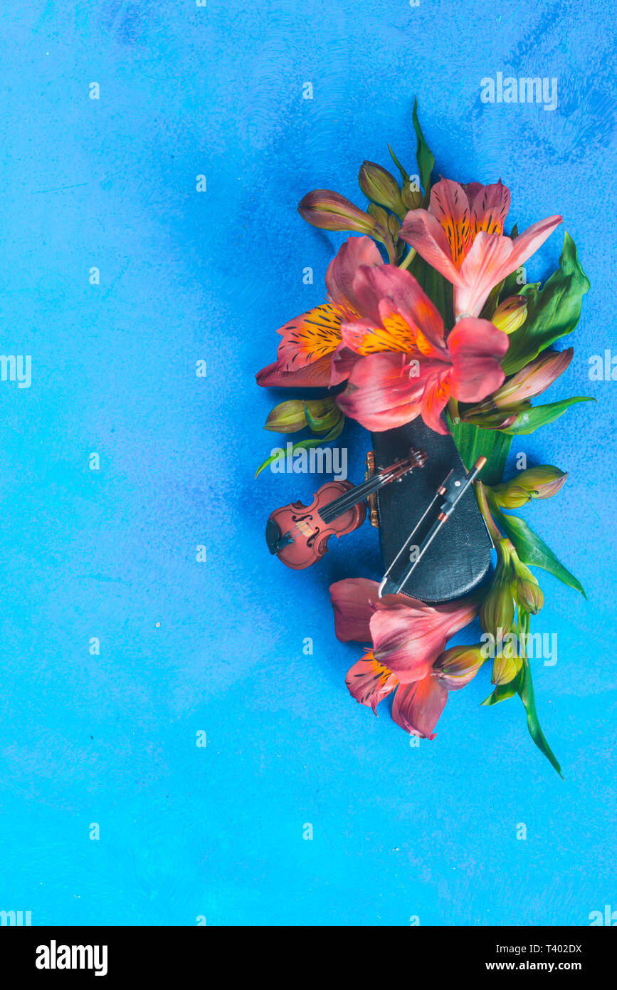 Kleine Geige mit Feder alstroemeria Blumen auf einem blauen Hintergrund mit kopieren. Frühling oder Sommer musikalische Festival Konzept mit Kopie Raum Stockfoto