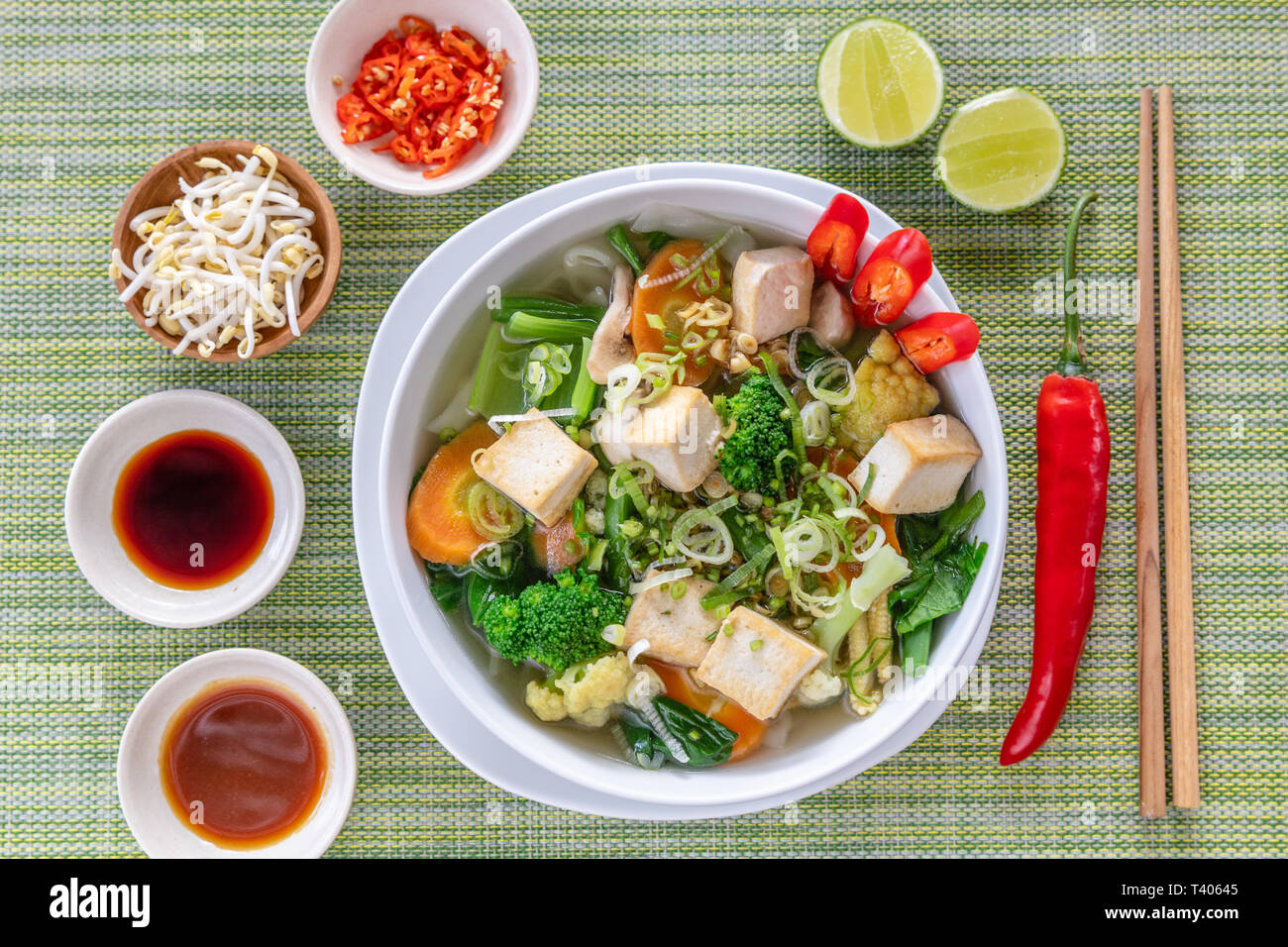Vegetarische vietnamesische Nudelsuppe Pho diente in Weiße, runde Schüssel, mit Saucen, Kalk, Chili und Sojasprossen. Holz- Stäbchen auf der Seite. Ansicht von oben. Stockfoto