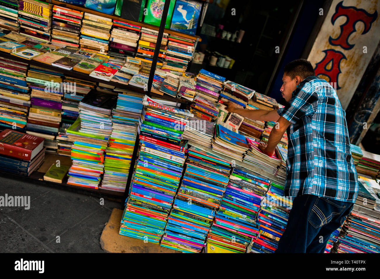Eine salvadorianische Buchhändler ordnet die Stapel der Bücher auf der Straße in einen gebrauchten Buchhandlung in San Salvador, El Salvador gestapelt. Stockfoto