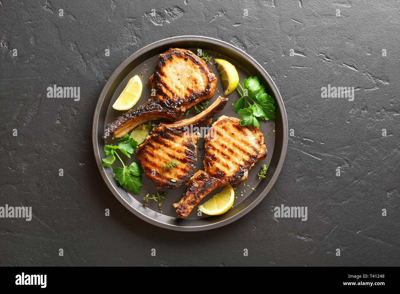Gegrilltes Schweinefleisch Steaks mit grünen und Zitrone auf die Platte über der schwarzen Stein Hintergrund mit kopieren. Ansicht von oben, flach Stockfoto