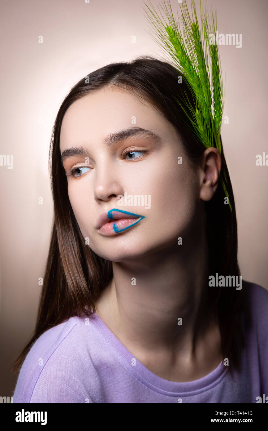 Attraktive Frau mit blauen Linien auf Lippen und grünen Ährchen im Haar Stockfoto