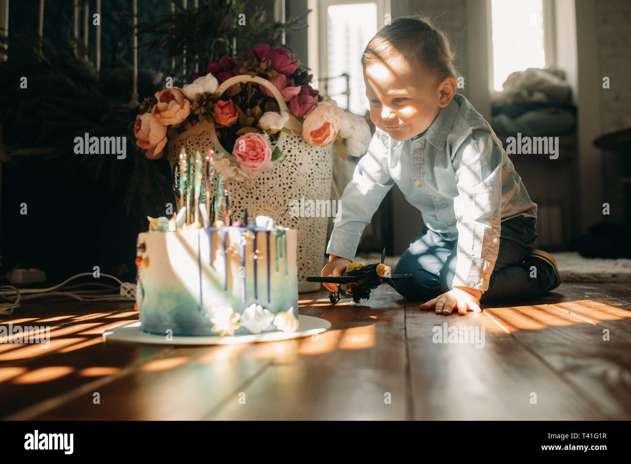 Kleinkind Junge sitzt auf dem Boden in der Nähe der Torte auf dem Hintergrund der Blumen. Stockfoto