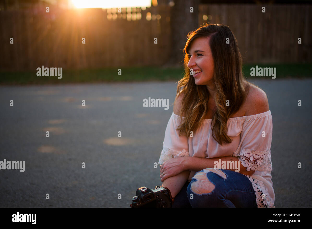 Ein schönes Lächeln Frau sitzt bei Sonnenuntergang mit Ihrer Kamera auf der Straße Stockfoto