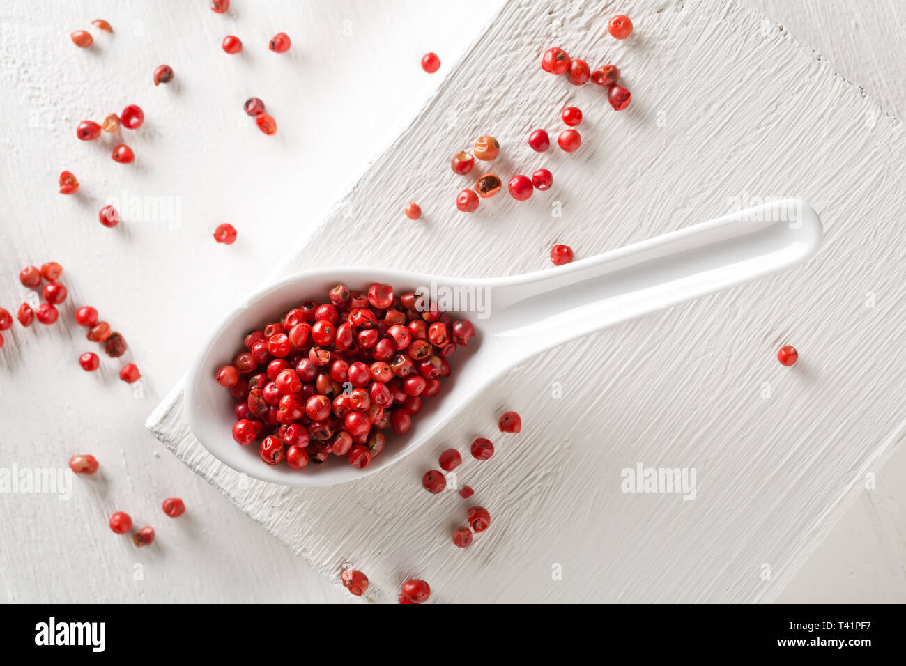 Pink oder Rosa brasilianischen roter Pfeffer (Schinus terebinthifolius) in Weiß Löffel auf weiße Holztisch Hintergrund - Flach top Aussicht von abov Stockfoto