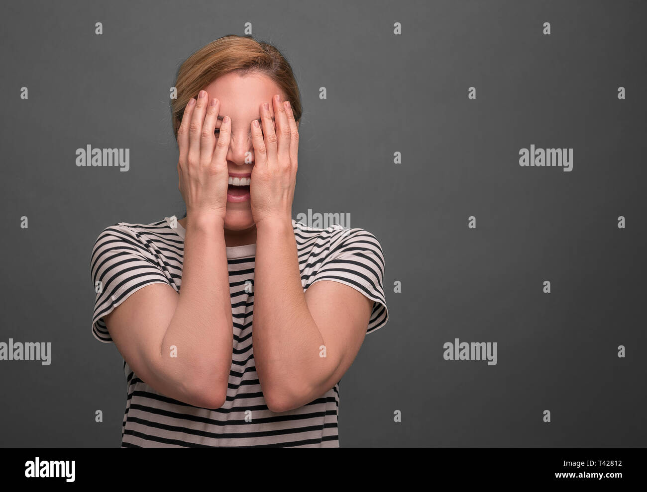 Junge Frau versteckt ihr Gesicht auf einem grauen Hintergrund. Stockfoto