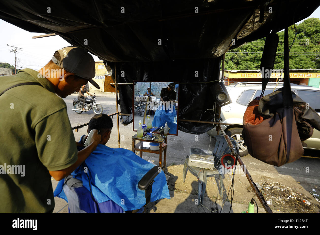 Valencia, Carabobo, Venezuela. 11 Apr, 2019. Pril 11, 2019. Gregory Hernandez, ist eine junge Venezolanische, die nicht mehr einen Job als Maurer, der seit vielen Jahren gewidmet war, beschlossen, eine lokale Straße, zu improvisieren und der Friseur- Service an solicarios Preise anbieten, die nach seinen eigenen Worten mindestens hilft Essen für Ihre Familie erhalten. Akzeptiert abgesehen von Bargeld oder elektronisches Geld, Pakete von Reis, Brot, Mehl, Teigwaren und anderen Lebensmitteln. Das Foto wurde auf Arantzasu Avenue, südlich der Stadt Valencia, Carabobo Zustand. Foto: Juan Carlos Hernandez (Credit Bild: © Juan Carlos Stockfoto