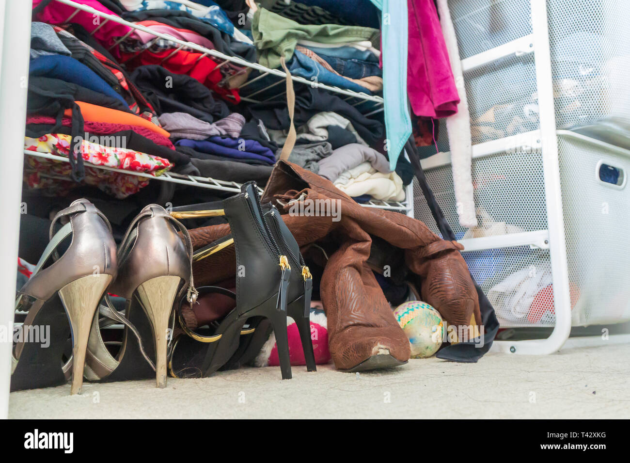 Schrank mit der Frau High Heel Schuhe, gestapelt, gefaltete Kleidung in den Regalen und Teil der hingen Bademäntel. Spiegel Schrank Organisation, spenden Kleidung. Stockfoto