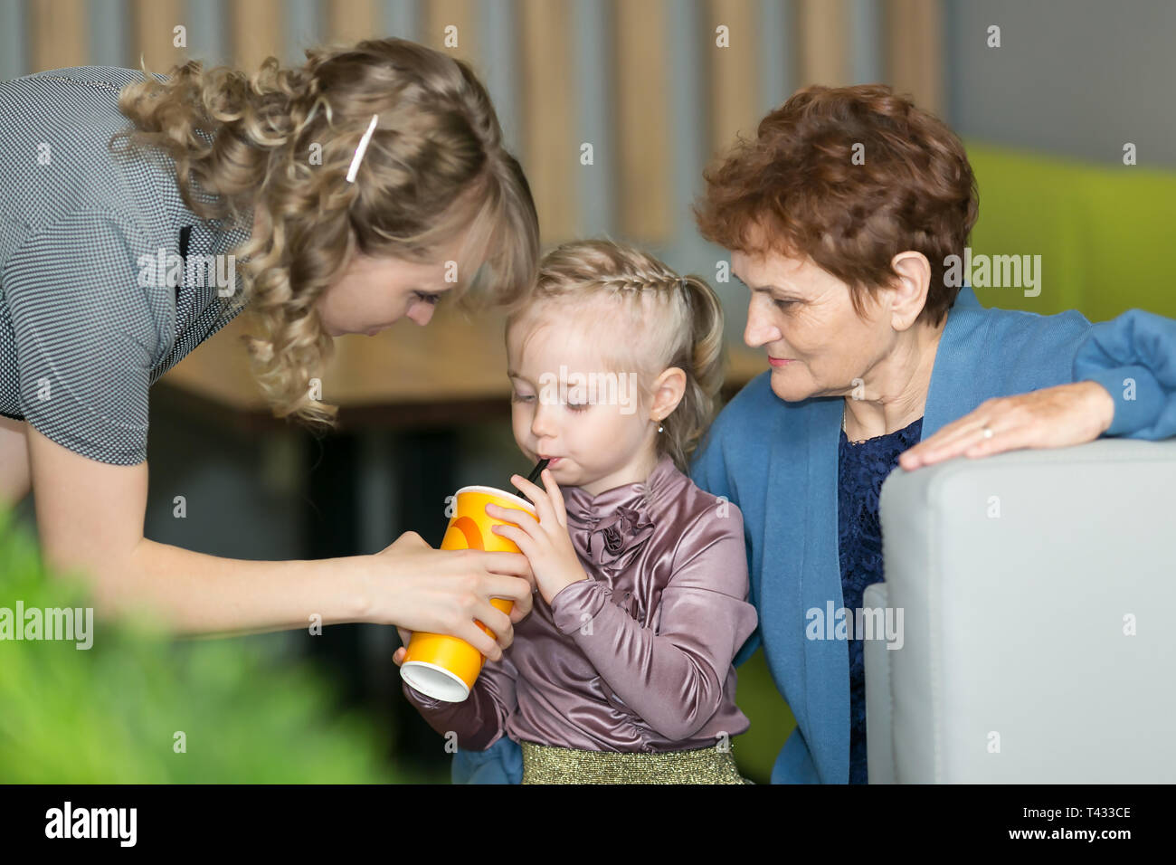 Eine junge Mutter hält ein Glas Wasser während der kleinen Tochter Getränke, und ihre Großmutter in der Nähe sitzt. Stockfoto