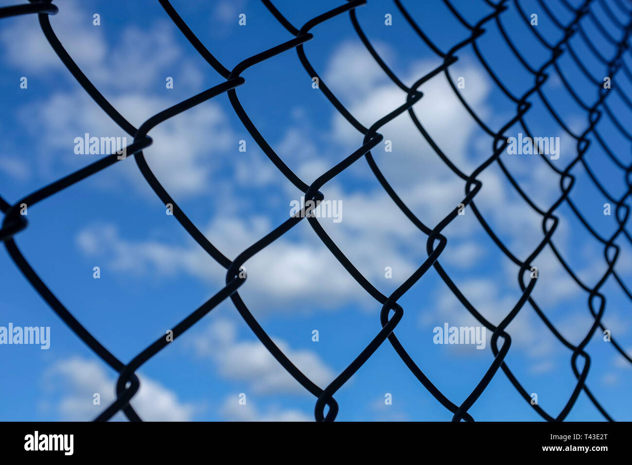 Blauer Himmel mit weißen Wolken durch eine chainlink Fence gesehen. Stockfoto