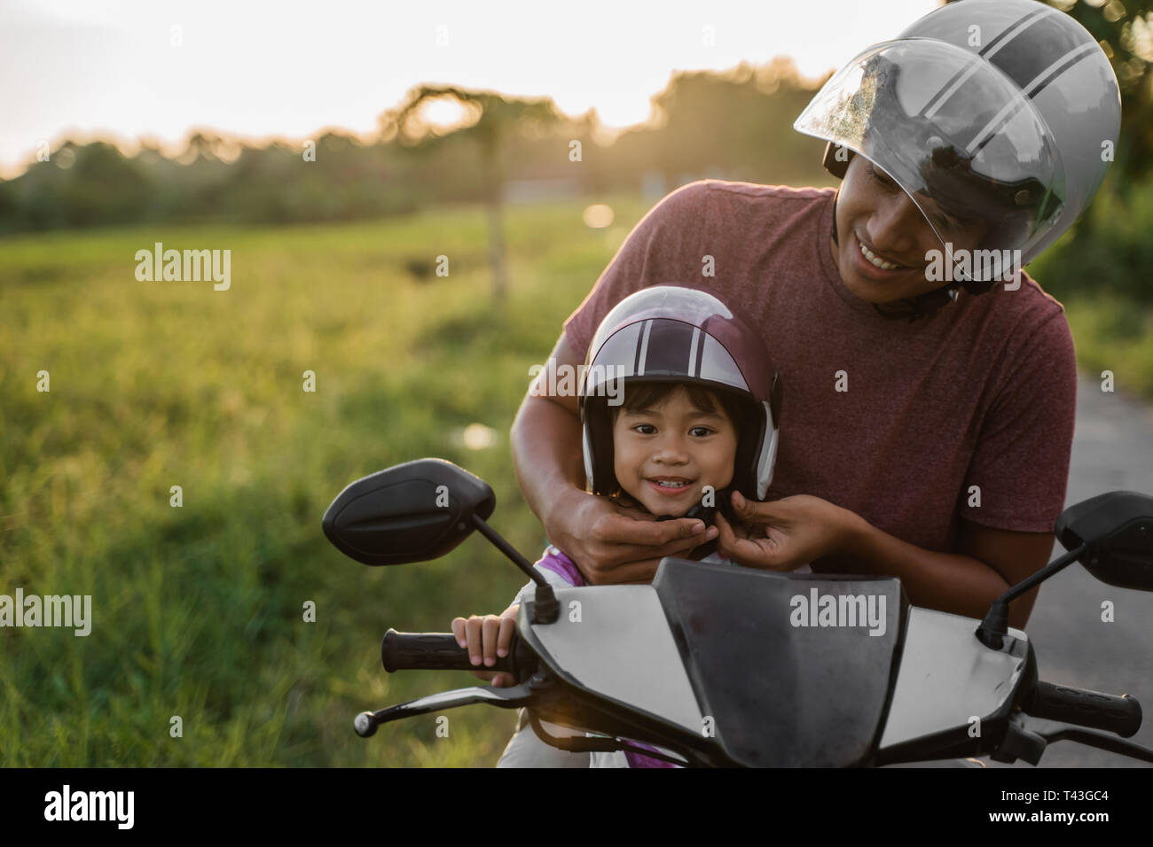 Papa helfen, ihre Tochter den Helm beim Reiten ein Motorrad Roller  befestigen Stockfotografie - Alamy