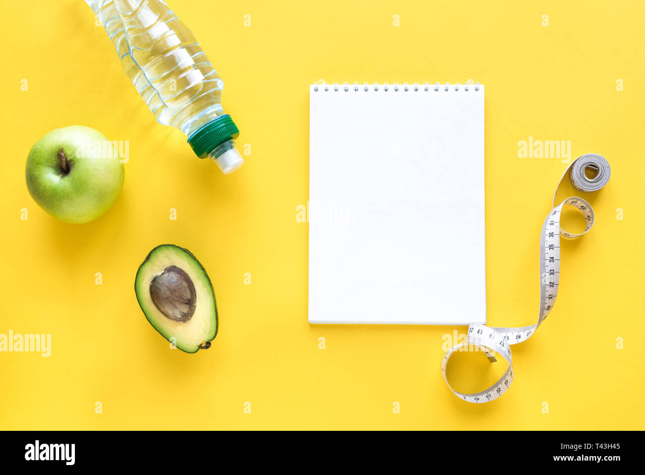 Gesunde Ernährung Konzept auf Gelb, Ansicht von oben, kopieren. Maßband, grüner Apfel, Avocado und Wasser für gesunde Ernährung und Gewichtsreduktion Diät. Stockfoto