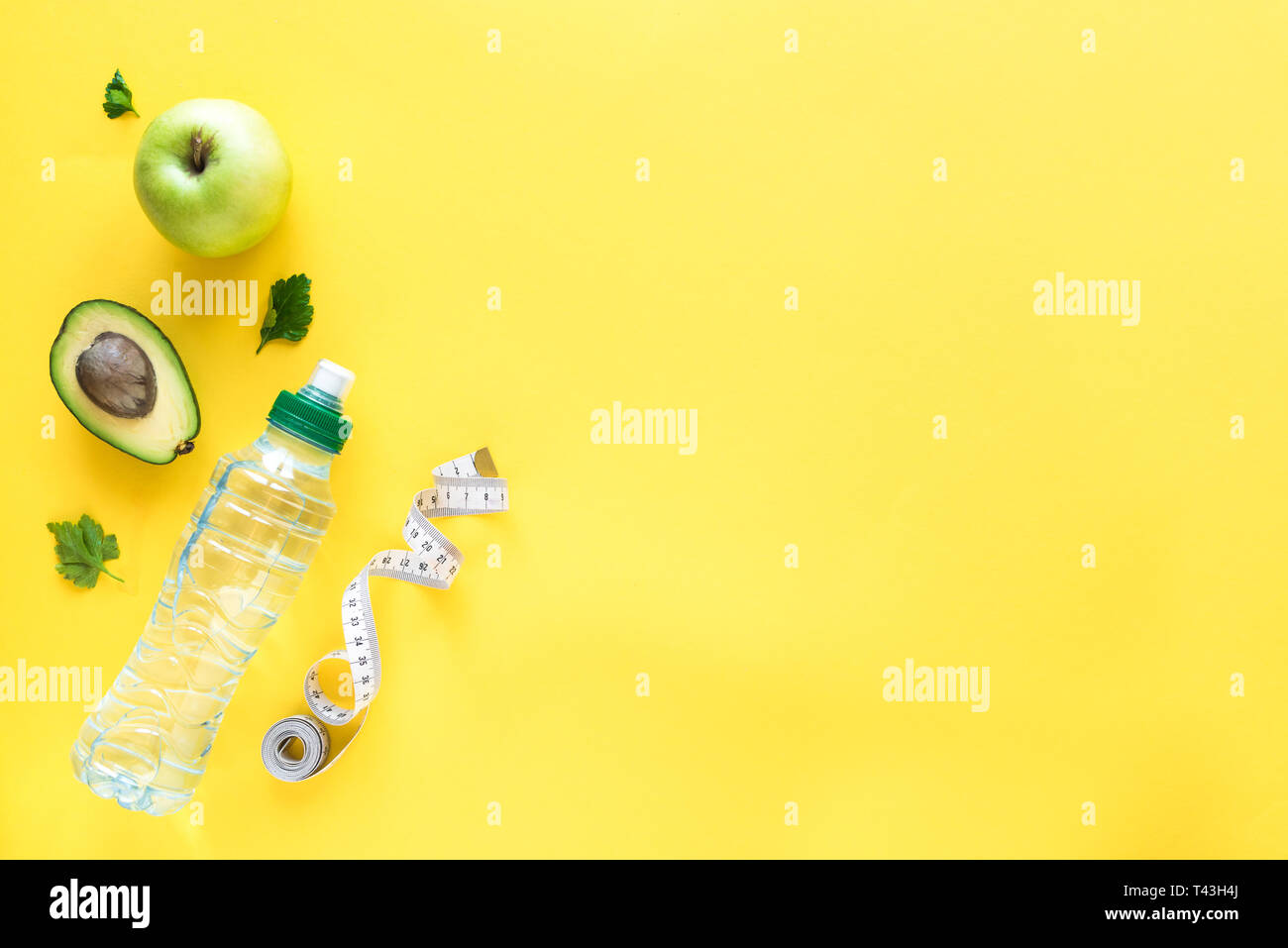 Gesunde Ernährung Konzept auf Gelb, Ansicht von oben, kopieren. Maßband, grüner Apfel, Avocado und Wasser für gesunde Ernährung und Gewichtsreduktion Diät. Stockfoto