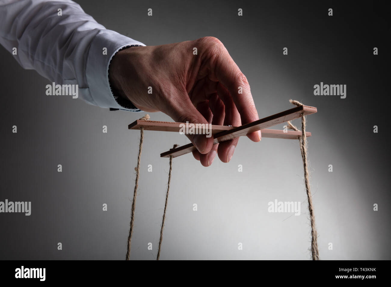Ein Geschäftsmann Hand manipulieren Marionette mit String gegen grauer Hintergrund Stockfoto