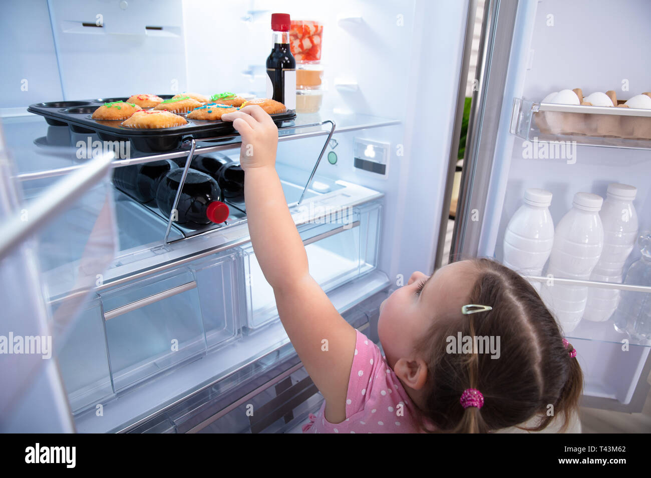 Süßes kleines Mädchen, die versuchen, zu erreichen, und kleine Kuchen aus  dem Kühlschrank zu Hause abholen Stockfotografie - Alamy