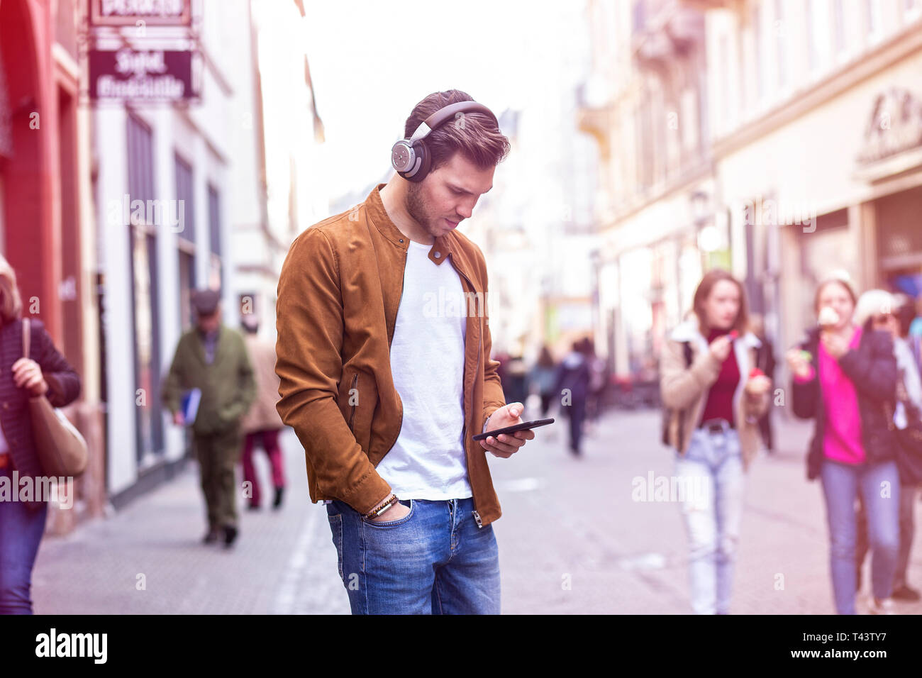 Junge Erwachsene charmanter Mann Musik hören und Sie ihr Smartphone auf der belebten Straße im Sommer Stockfoto
