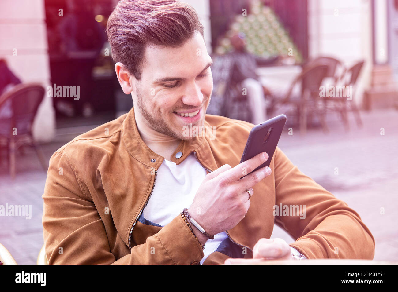 Glückliche junge Erwachsene charmante Mann auf dem Smartphone auf öffentlichen Café Terrasse Stockfoto