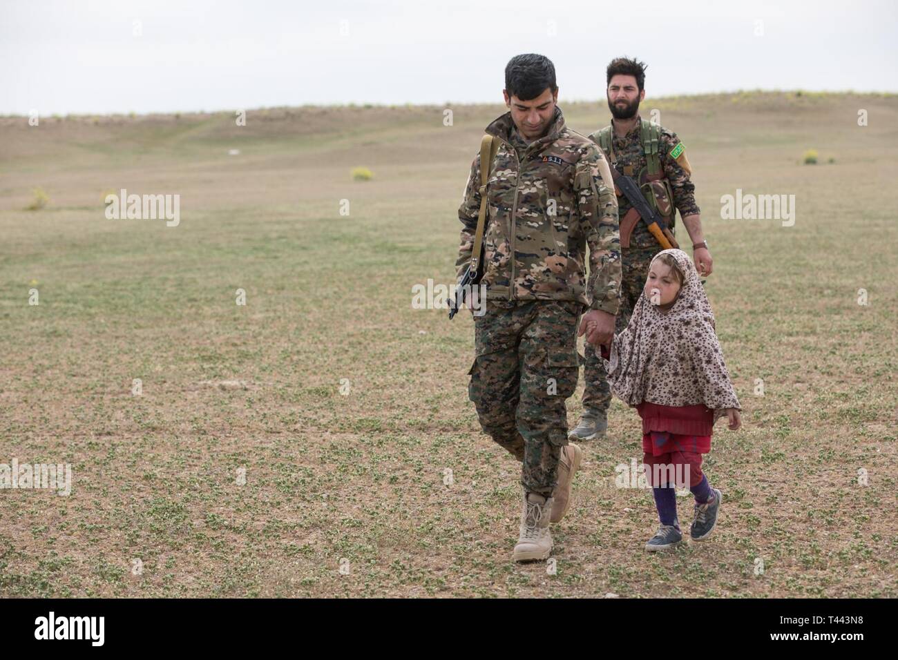 Syrisch demokratischen Kräfte Mitglieder escort ein Kind eines Verzichts Daesh Mitglied während einer SDF-led-Screening und biometrische Anmeldung im Deir ez-Zor Provinz, Syrien, März 13, 2019. Die Kampagne des Daesh von Zerstörung und Brutalität zerstört das Leben der großen Anzahl und vertriebenen Tausende. CJTF-OIR Mission ist Daesh in ausgewiesenen Teile des Irak und Syrien zu besiegen, und für festgelegte Bedingungen für den Betrieb der regionalen Stabilität zu erhöhen. Stockfoto