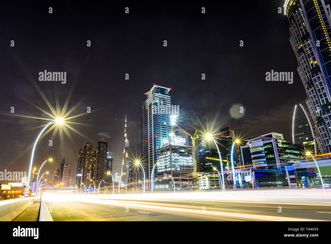 Atemberaubende Aussicht auf die beleuchtete Skyline von Dubai bei Nacht mit den herrlichen Burj Khalifa im Hintergrund und einer sehr befahrenen Straße mit leichten Wanderwegen. Stockfoto