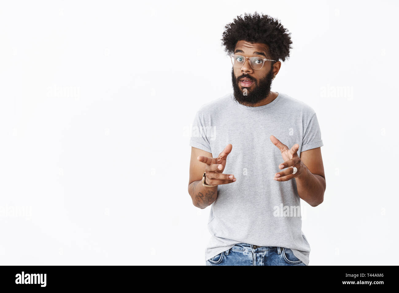 Stattliche männliche Bärtigen african american man in Gläsern mit Tätowierungen Gestik und winkende Hände wie Sprechen, die erklären, wie die Arbeit, mit der sie die Auge Stockfoto