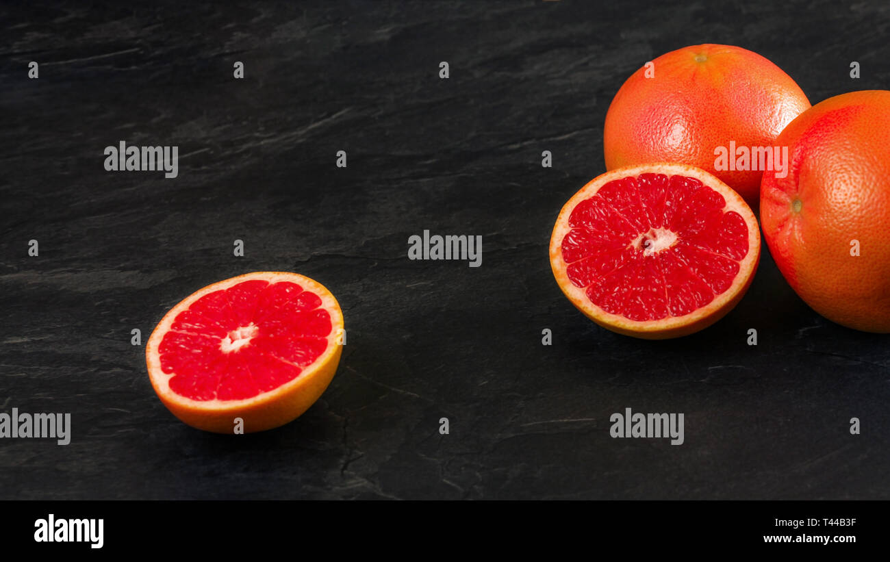 Rosa Grapefruits, eine Frucht halbiert, auf schwarzem Schiefer wie Vorstand, breiten Raum für Text, Foto, linke Seite Stockfoto