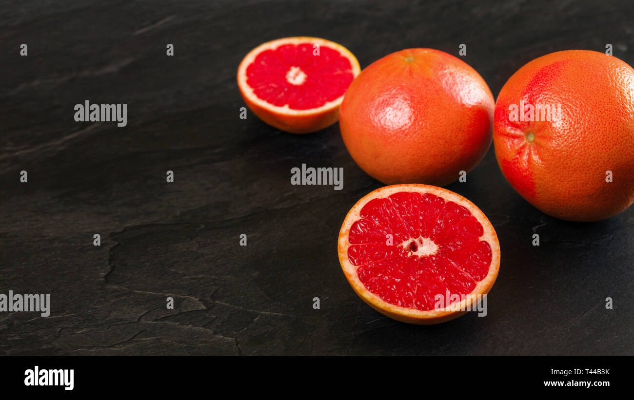 Rosa Rot Grapefruits, einer Zitrusfrucht halbieren, auf schwarzem Schiefer wie Vorstand, breite Foto mit leeren Raum für Text, linke Seite Stockfoto