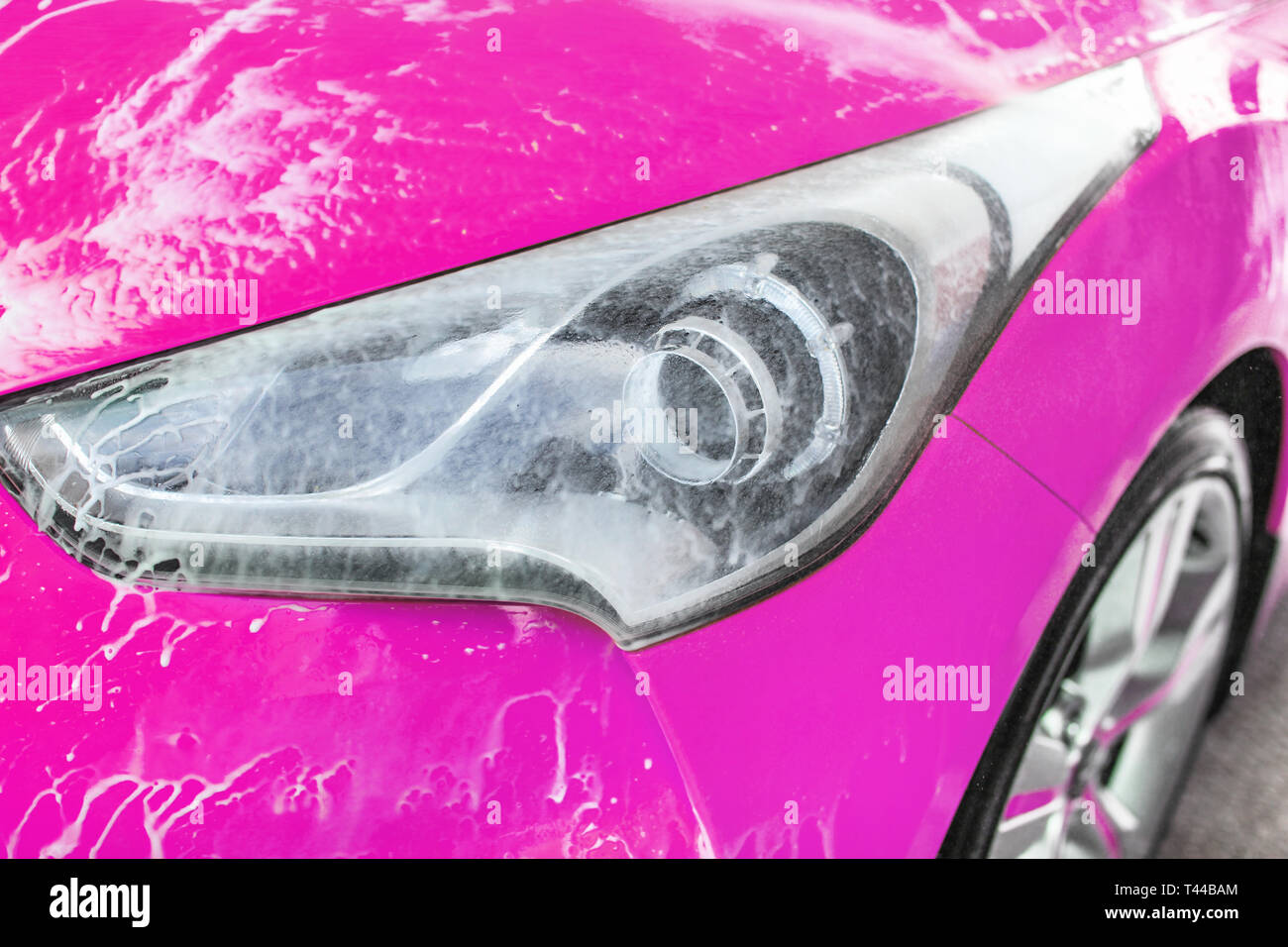 Vordere Scheinwerfer von Rosa Auto in selbst gewaschen dienen Carwash, Wasser spritzen Blätter weißer Schaum auf Glas Stockfoto