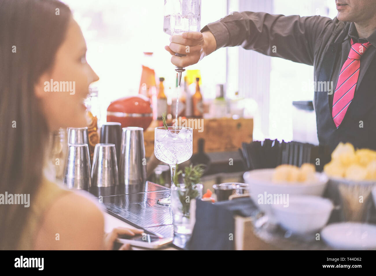Junge Frau ihr Getränk an der Theke warten - professionelle Bartender einen Cocktail zu Menschen in der amerikanischen Bar, Außenpool Stockfoto