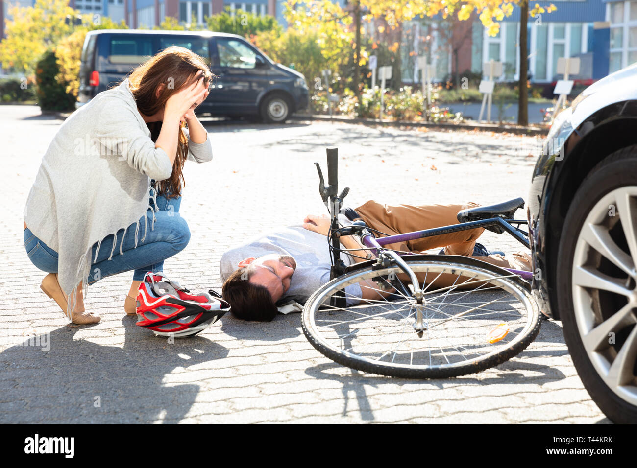 Junge Frau auf Unbewussten männlichen Radfahrer liegen an der Straße nach Unfall in der Nähe von Auto Stockfoto
