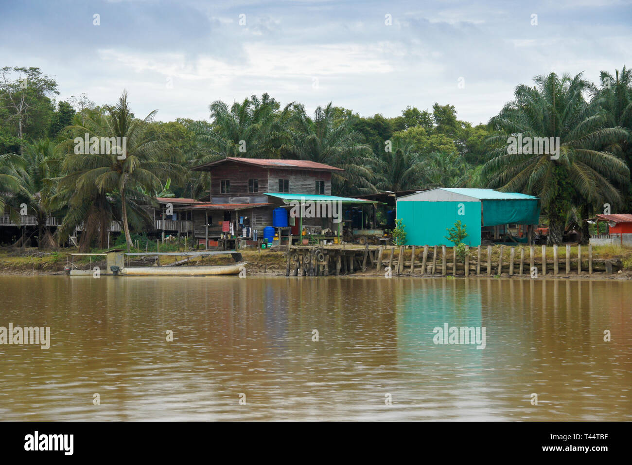 Häuser und Boot am Ufer des Kinabatangan Flusses (Sungai Kinabatangan) in der Nähe von Sukau, Sabah (Borneo), Malaysia Stockfoto