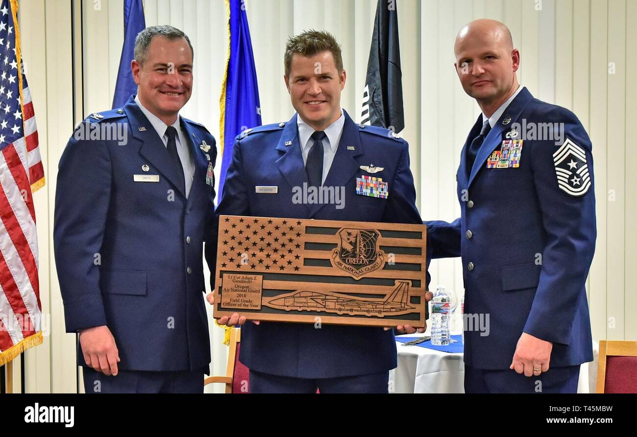 Us Air Force Oberstleutnant Adam Gaudinski, 173Rd Operations, wird als die Oregon Air National Guard Field Grade Officer des Jahres während einer Zeremonie in Klamath Falls, Oregon, 2. März 2019 hielt geehrt. Die 173Rd Fighter Wing Commander, Col. Jeff Smith, und die 173Rd FW-Befehl Chief, Chief Master Sgt. Dominic Ingle, stellte ihm eine Personalisierte Plakette im Namen des Staates. Stockfoto