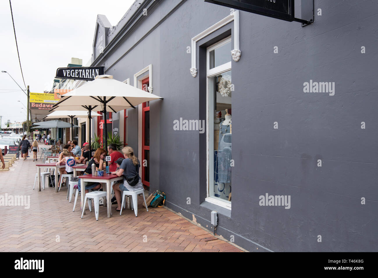 Die Menschen essen unter Sonnenschirmen auf dem Fußweg außerhalb Pilger Vegetarian Cafe in Milton an der Südküste von New South Wales, Australien Stockfoto