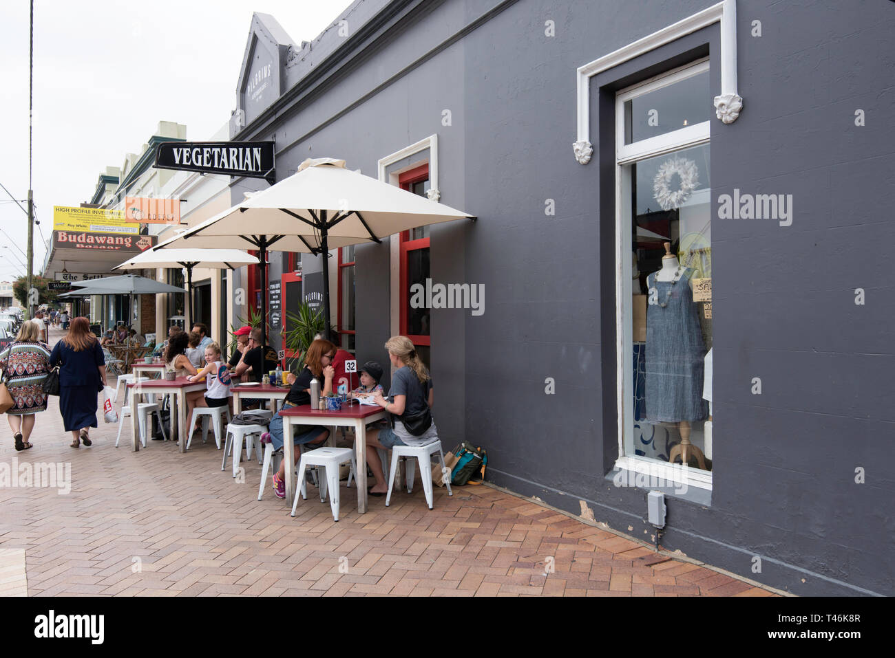 Die Menschen essen unter Sonnenschirmen auf dem Fußweg außerhalb Pilger Vegetarian Cafe in Milton an der Südküste von New South Wales, Australien Stockfoto