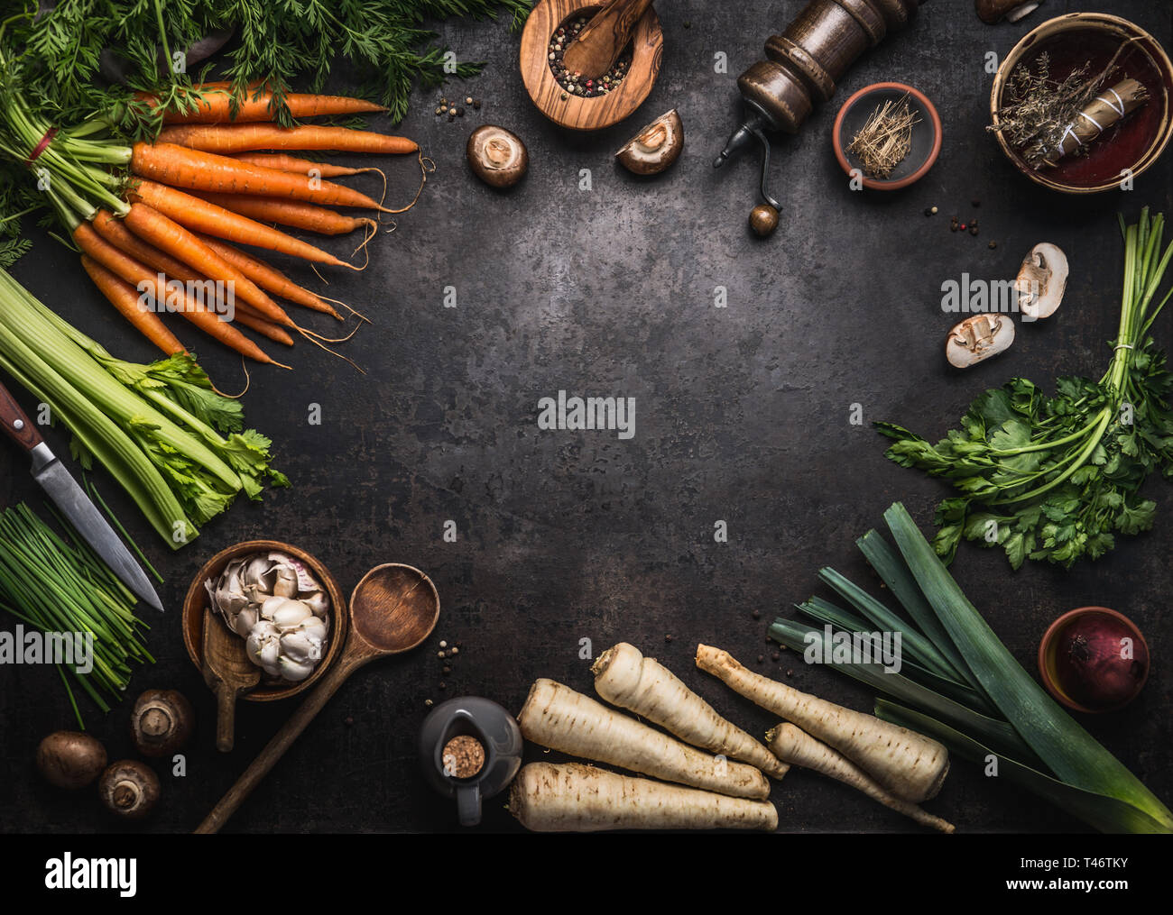 Essen Hintergrund mit verschiedenen organischen Farm Gemüse auf dunklen rustikalen Tisch mit Küchengeräten, Kräuter und Gewürze, Ansicht von oben. Rahmen. Kopieren Sie Platz. Vegan Stockfoto
