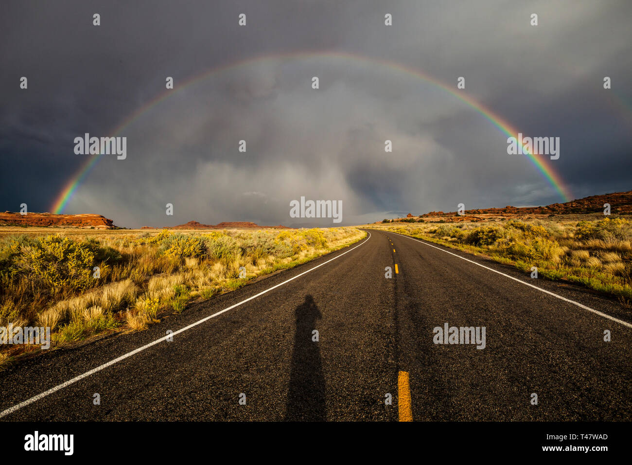 Der Schatten der Fotograf zeigt auf der Straße unter einem Regenbogen und thuderstorm Wolken über Scenic Highway 211 im Canyonlands National Park, Sou Stockfoto