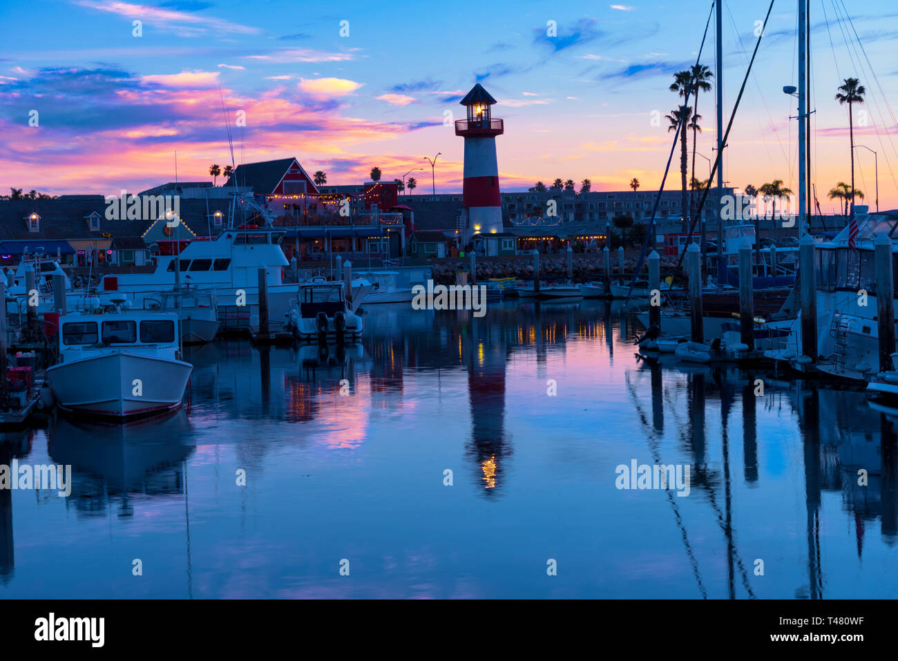 Sonnenuntergang mit Rosa, Rot, Gelb und Blau Skier über Hafen und Leuchtturm Boote, Wasser Reflexion der Himmel. und den Leuchtturm. Stockfoto