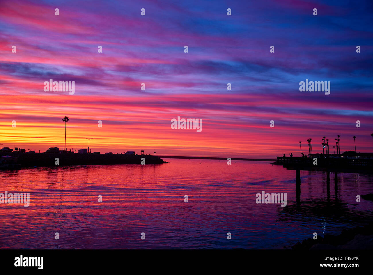 Hafeneinfahrt widersteht Silhouetten gegen einen Himmel von Blau, Violett, Rot, Orange und Gelb. Der Ozean ist reelecting die Farben des Himmels. Stockfoto