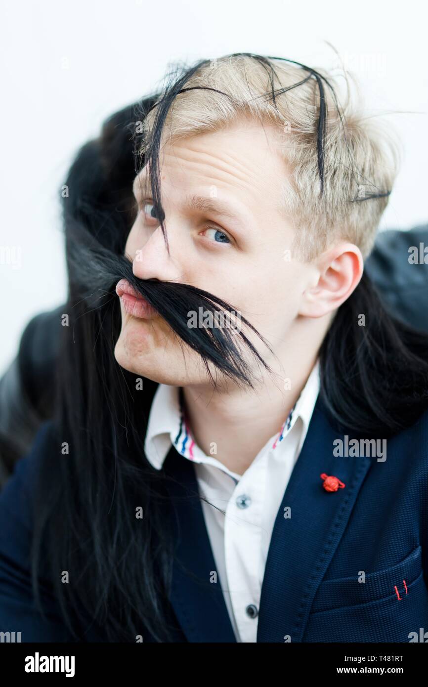 Blonder Mann in formelle Kleidung macht lustig mit gefälschten Schnurrbart von Haare schwarz Freundin Grimasse. Stockfoto