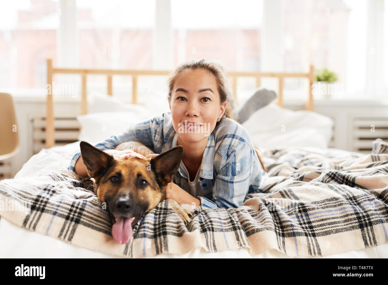Junge asiatische Frau posiert mit Hund auf dem Bett Stockfoto