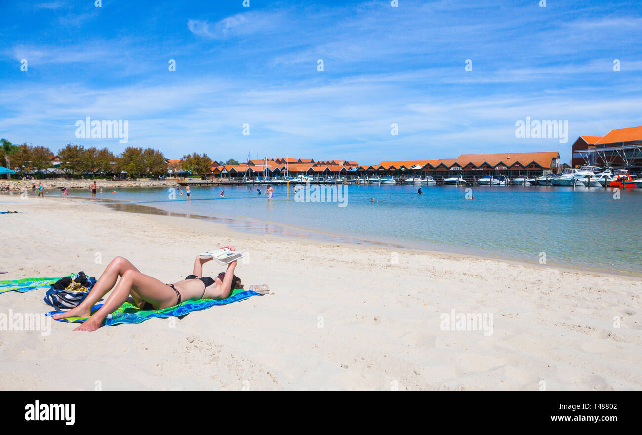 Ein junges Mädchen Sonnenbaden und Lesen ein Buch am Strand von Sorrent Quay Hillarys Boat Harbour. Stockfoto